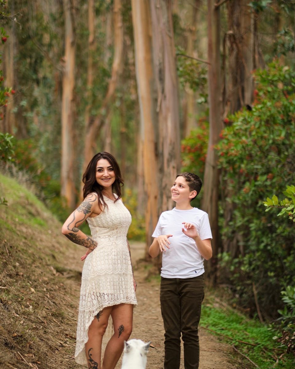 Cheryl Scorza walking a wooded trail with her son and their white dog, Roo.