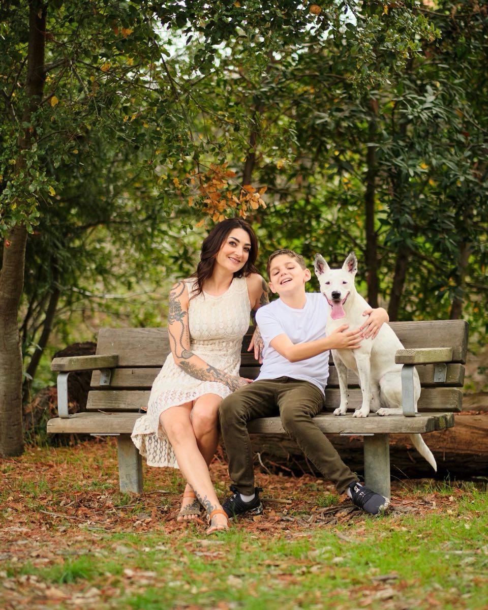 Cheryl Scorza on a bench with her son and their white dog, Roo.