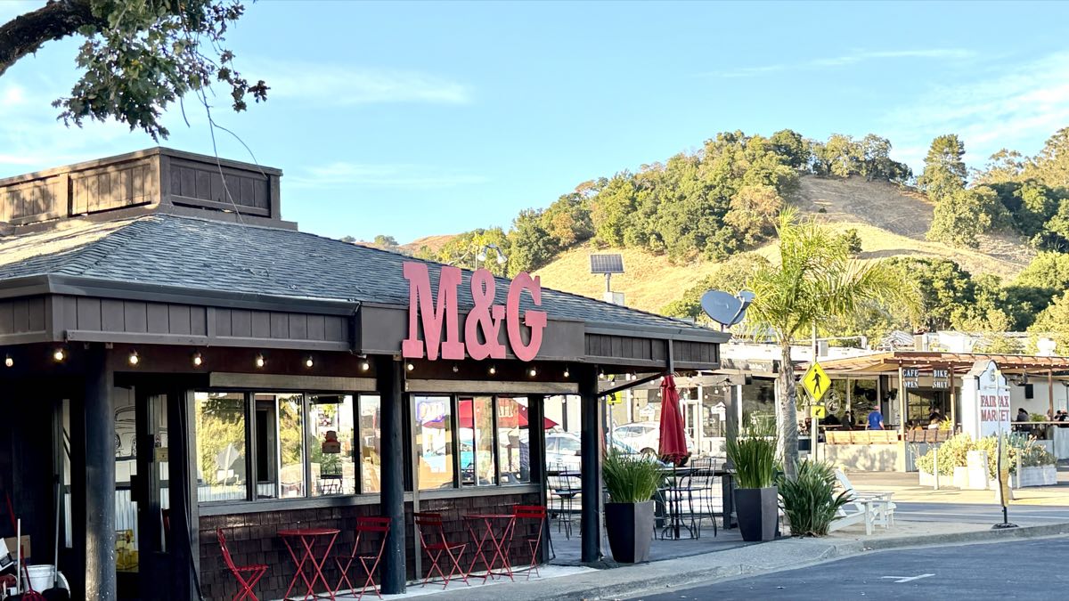 M&G's on Sir Francis Drake, open, with red tables out on the sidewalk and the dry hills behind.