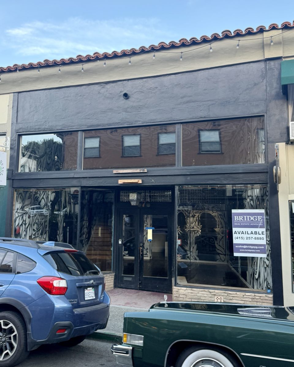 An empty storefront on Bolinas Road with a black painted frontage and an agent's AVAILABLE sign in the window.